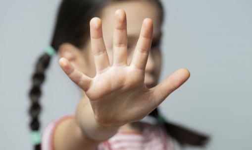 Six year old girl showing stop gesture while standing against gray background.